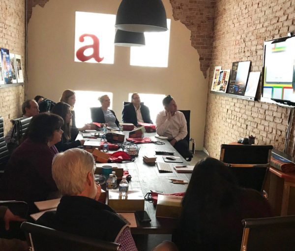 A group of AcrobatAnt employees seated around a conference room table watching a TV.