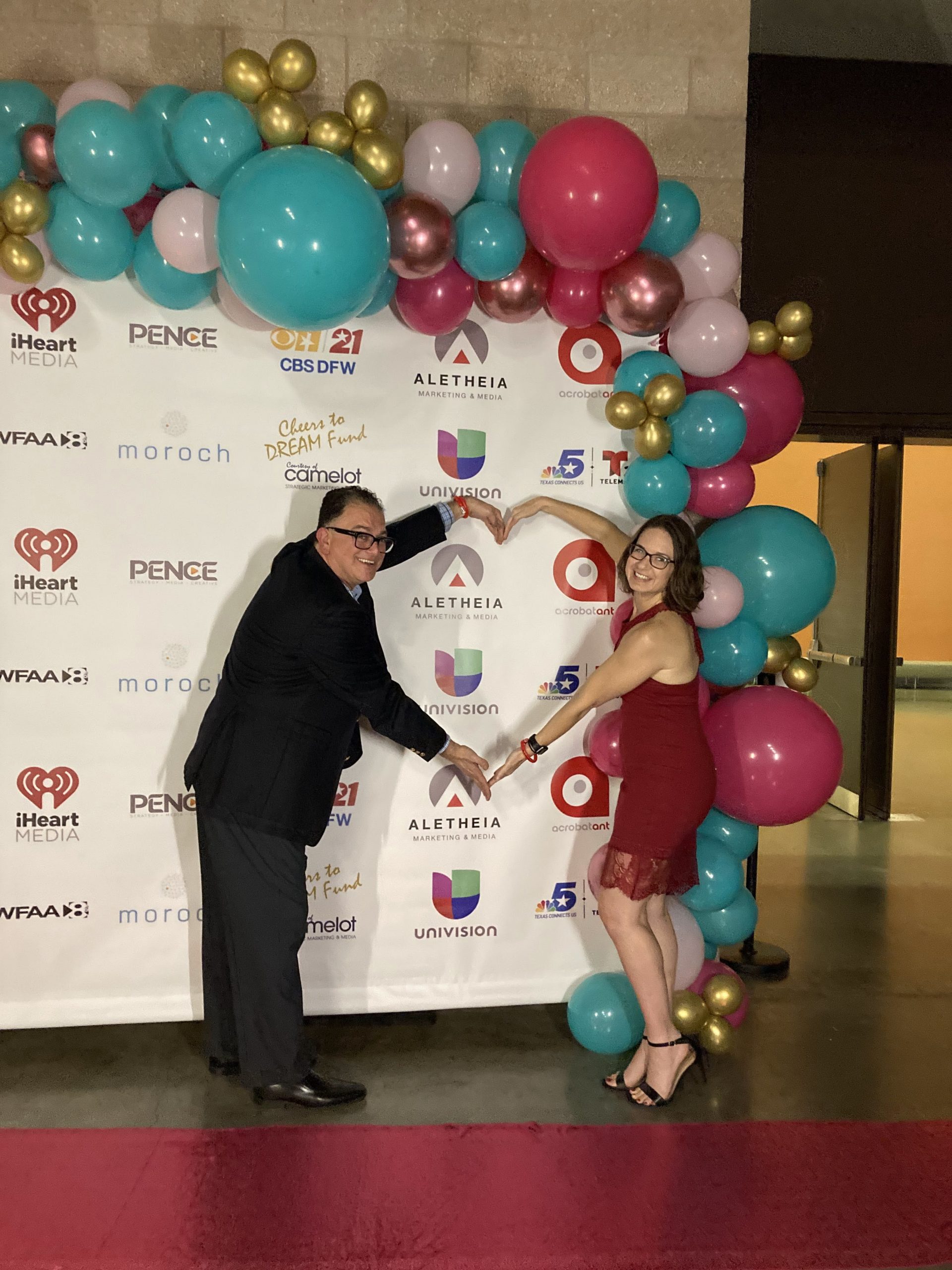 Two people holding arms together in the shape of a heart with balloons in foreground.