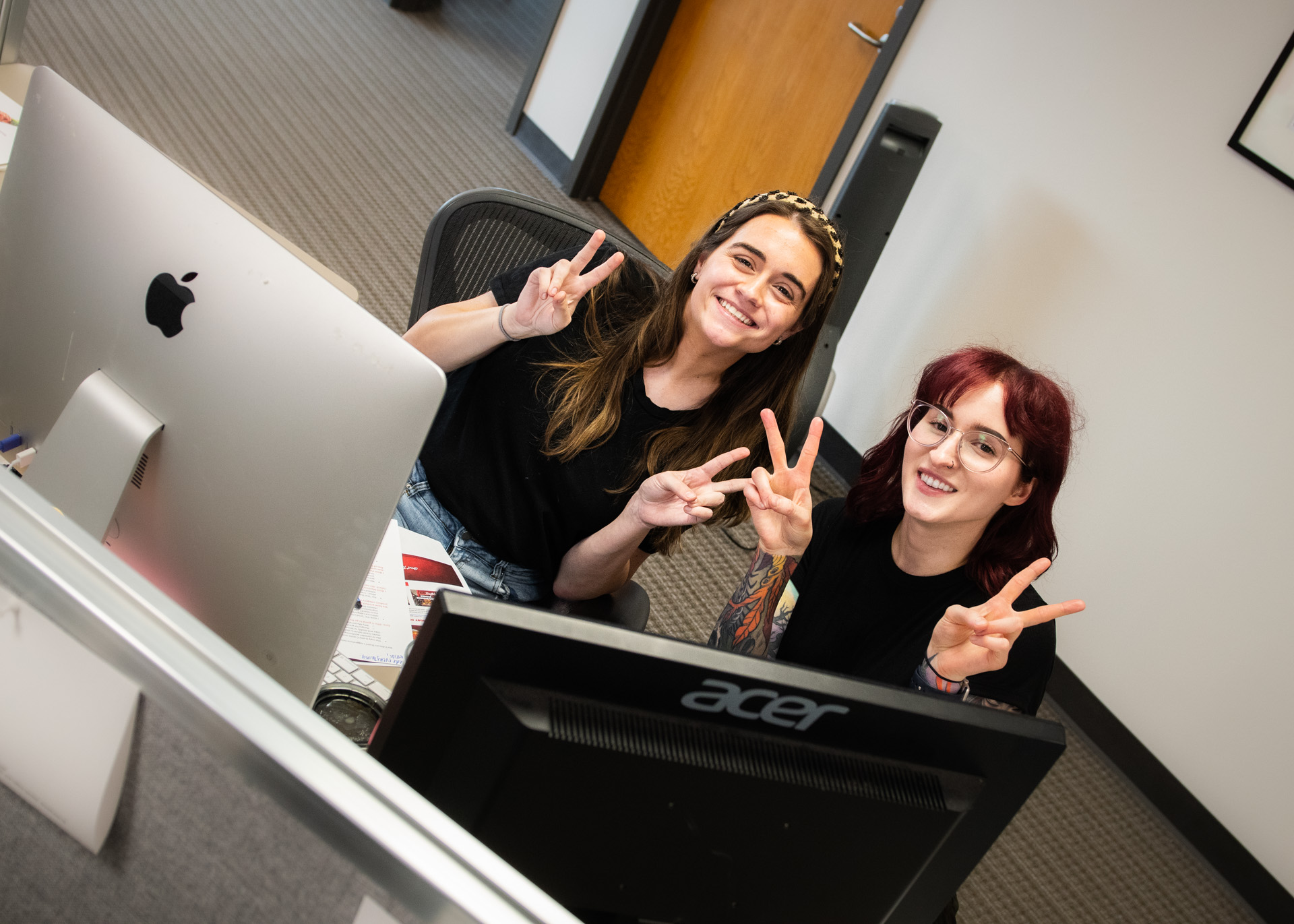 Two girls smiling in an office with peace signs