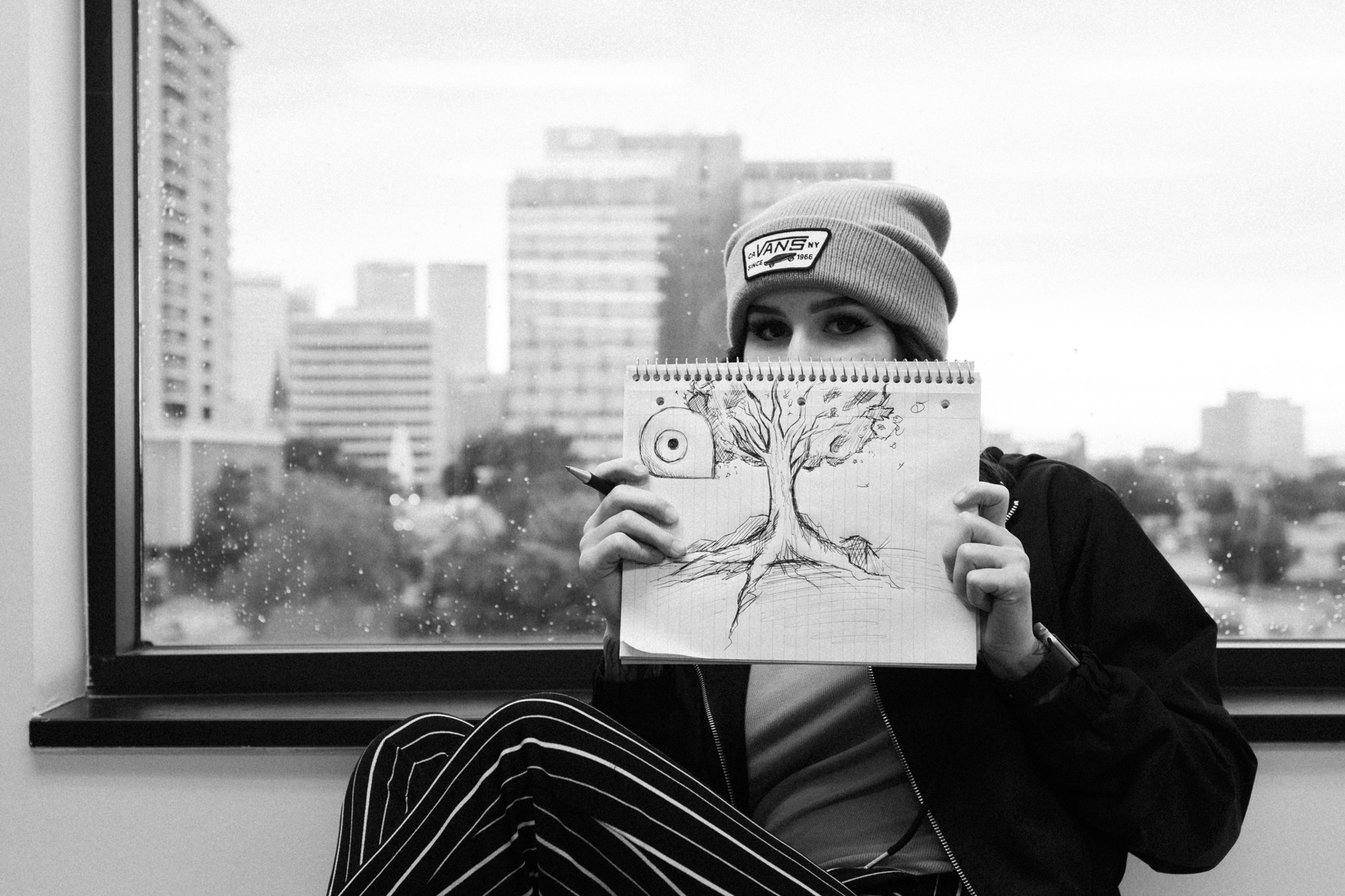 girl in beanie holding g sketch of tree