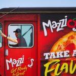 A man in a red Mazzio's food truck that reads "Mazzios, Take a Flavor Trip, Street Pizza"