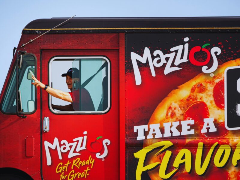 A man in a red Mazzio's food truck that reads "Mazzios, Take a Flavor Trip, Street Pizza"